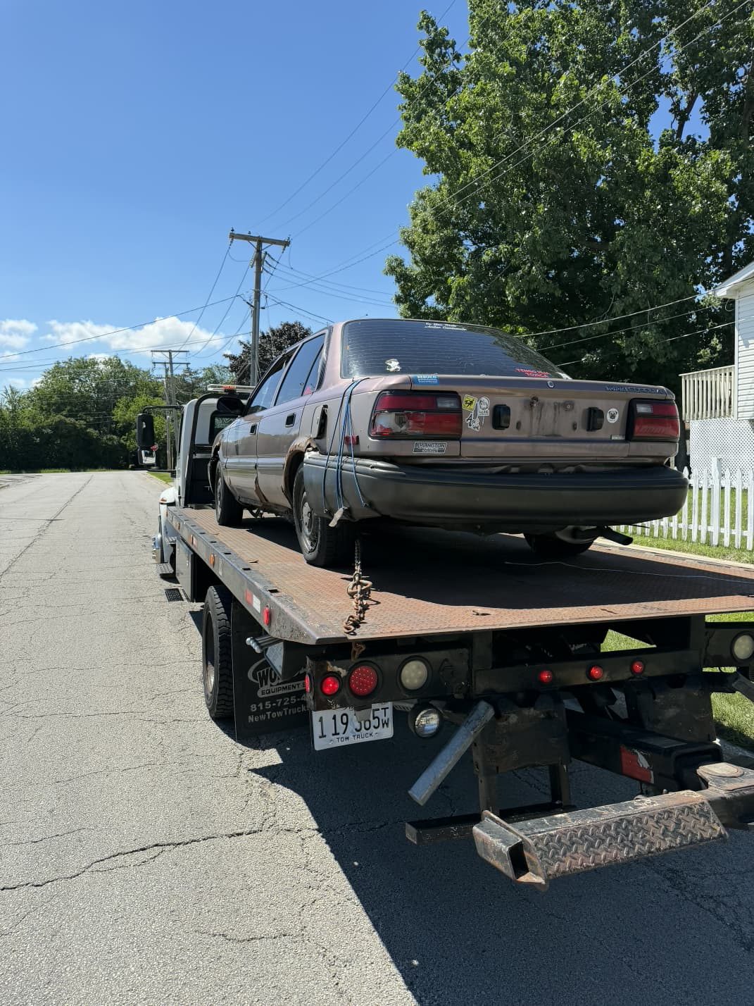 Junk sedan strapped down on a flatbed tow truck during pickup